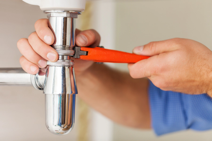 worker repiping some pipes of a sink with an orange plumbing tool